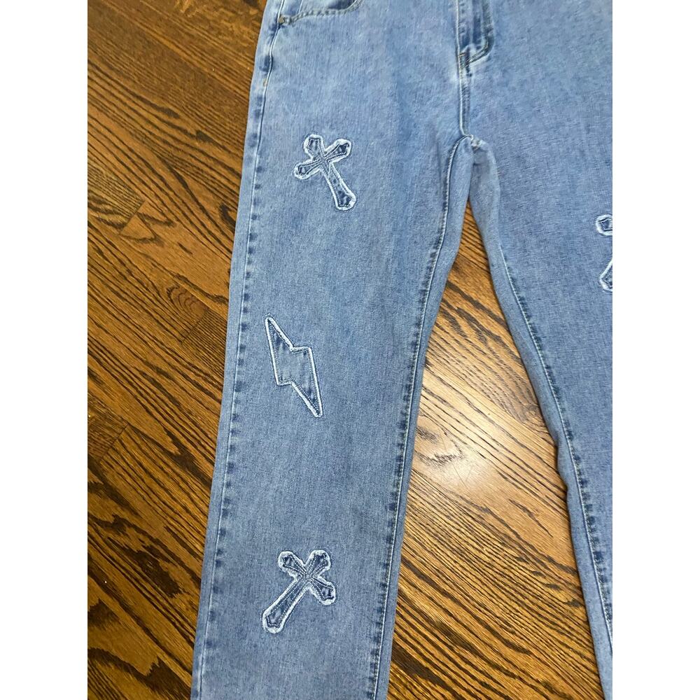 Light wash denim jeans with cross and lightning bolts appliqué